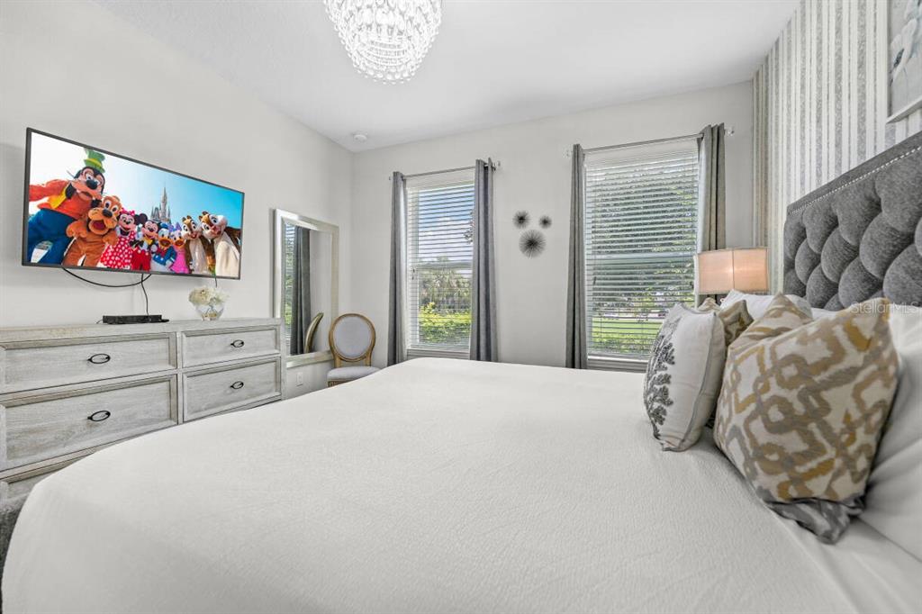 A bedroom features a king bed, a light wood dresser, and a wall-mounted television — 1804 SANDY PARK TRAIL, KISSIMMEE, FL