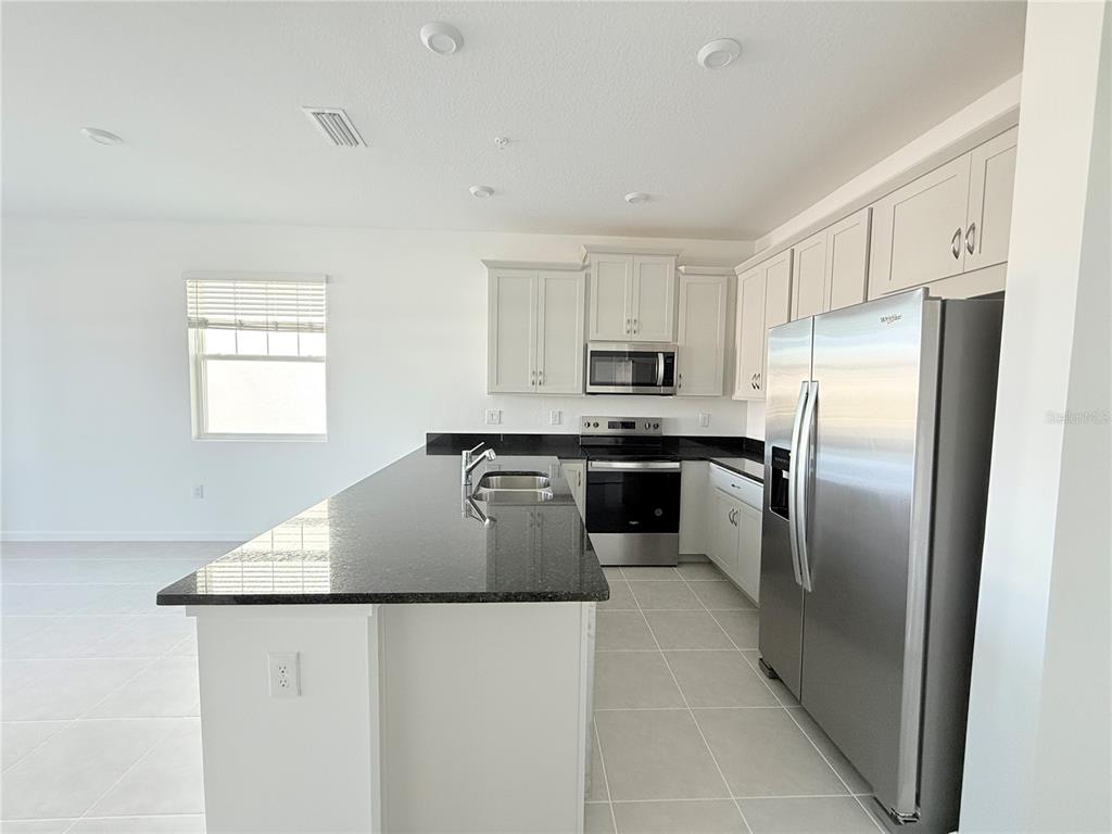 A kitchen with white cabinets, black countertops, stainless steel appliances, and light tile flooring — 4124 SADLER ROAD, APOPKA, FL