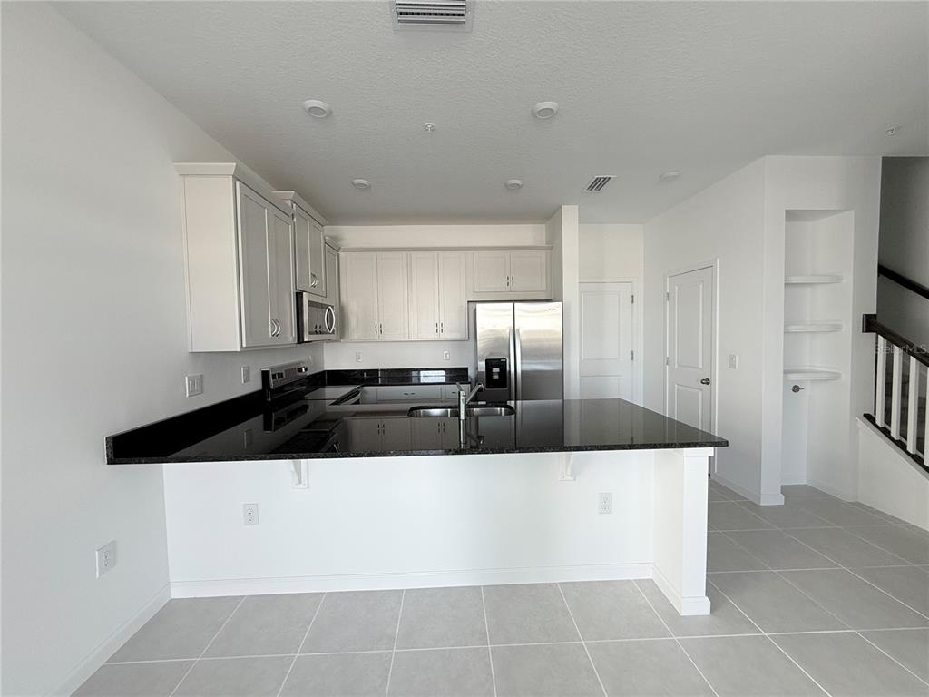 A kitchen features white cabinets, black countertops, stainless steel appliances, and light gray tile flooring — 4124 SADLER ROAD, APOPKA, FL