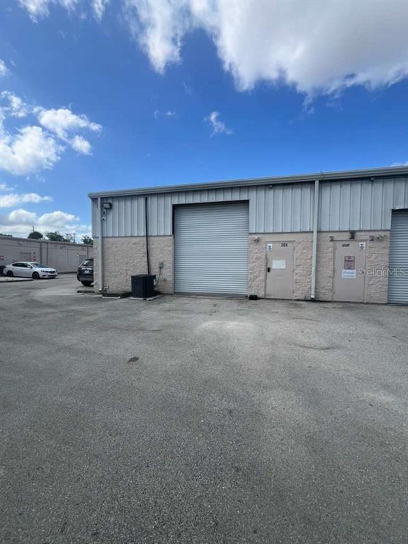 An exterior view of a commercial warehouse building with a roll-up door and two entry doors — 11601 S ORANGE BLOSSOM TRAIL UNIT 201, ORLANDO, FL