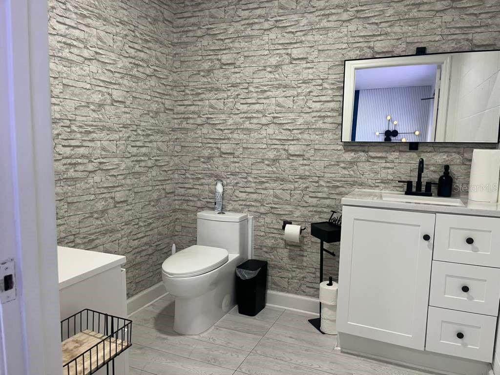 A bathroom features a stone-look accent wall, a white vanity, and a toilet — 11601 S ORANGE BLOSSOM TRAIL UNIT 201, ORLANDO, FL