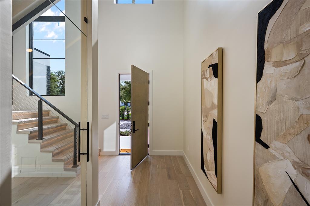 A modern entryway features light wood floors, a staircase with cable railings, and abstract wall art — 525 S LAKEMONT AVENUE, WINTER PARK, FL
