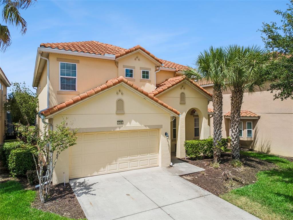 A two-story stucco house features a tile roof, a two-car garage, and palm trees — 4348 ACORN COURT, DAVENPORT, FL