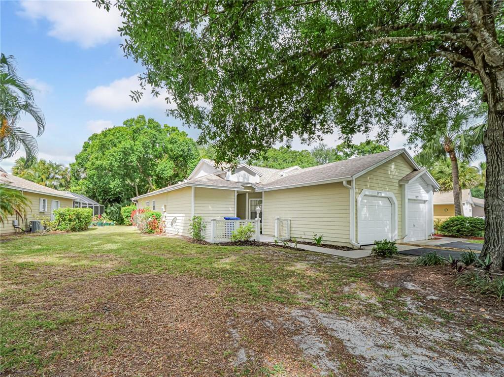 A light yellow single-story house with a two-car garage and a large grassy yard — 1875 Sixty Oaks Lane, Vero Beach FL 32966, VERO BEACH, FL