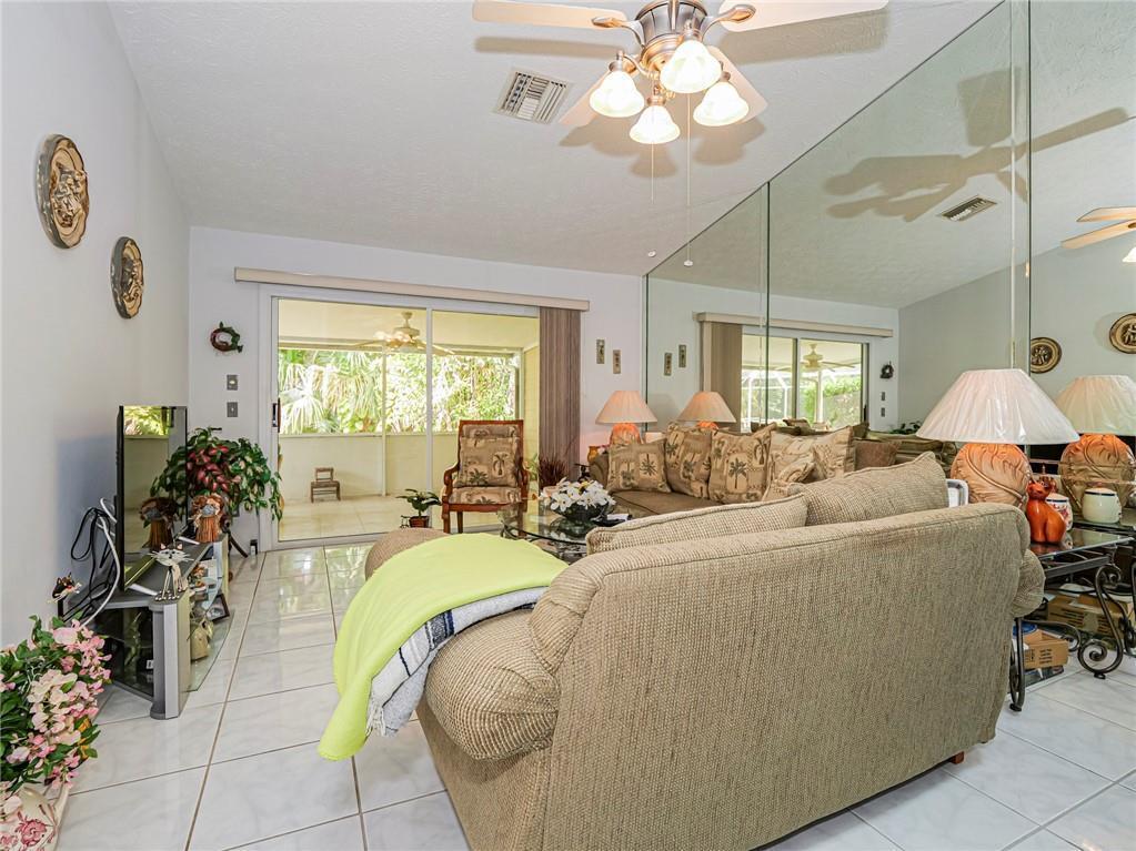 A living room features tiled floors, a mirrored wall, a ceiling fan, and sliding glass doors — 1875 Sixty Oaks Lane, Vero Beach FL 32966, VERO BEACH, FL