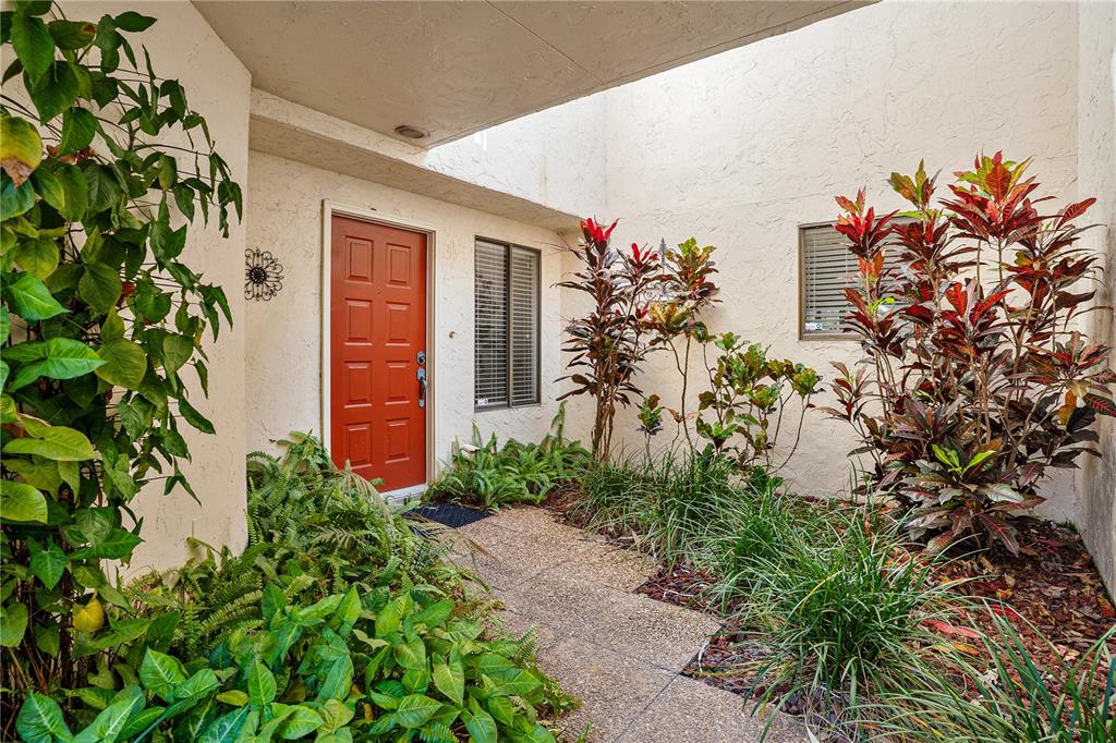 A red front door is set within a landscaped courtyard with a covered walkway — 402 CLUSTERWOOD DRIVE, YALAHA, FL