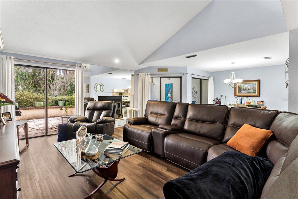 A living room features a vaulted ceiling, brown leather furniture, and sliding glass doors — 402 CLUSTERWOOD DRIVE, YALAHA, FL