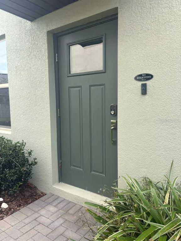 A green front door with a window and electronic lock is set in a stucco wall — 21834 ADRIATIC LANE, LAND O LAKES, FL