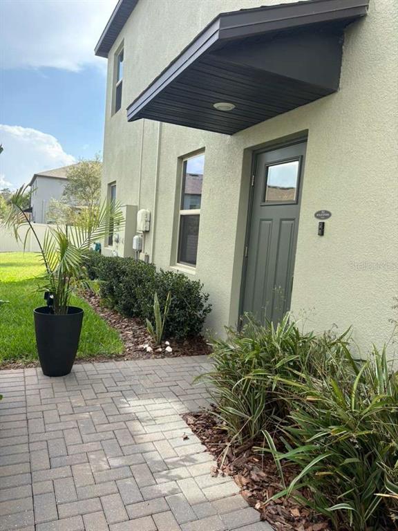 A paved walkway leads to a green door under a dark awning on a stucco house — 21834 ADRIATIC LANE, LAND O LAKES, FL