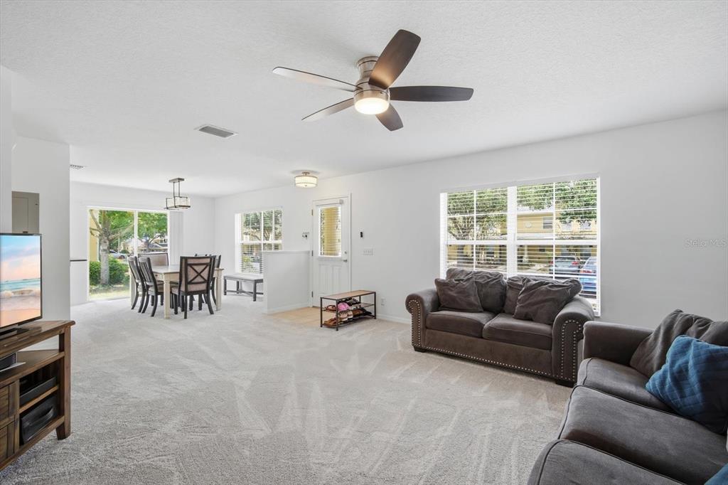 A living room and dining area with carpeted floors, a ceiling fan, and large windows — 3435 CASTLE STONE COURT, VALRICO, FL