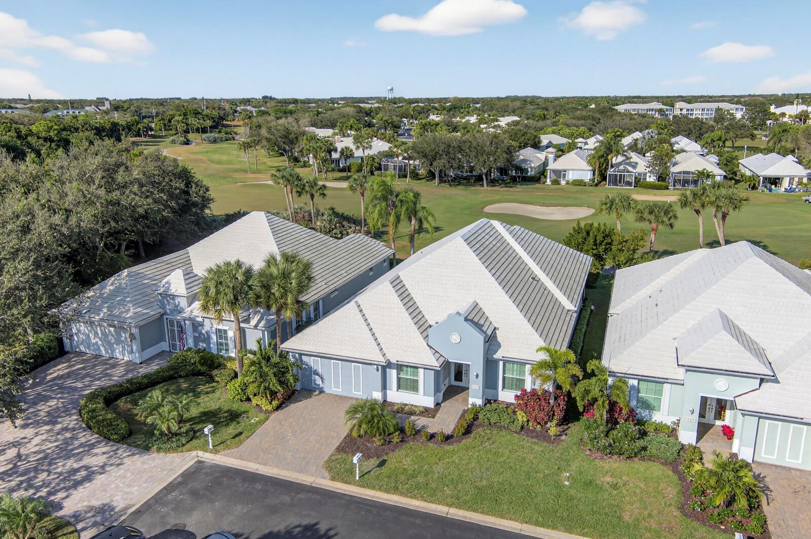 An aerial view shows three suburban houses with tiled roofs situated along a golf course — VERO BEACH, FL