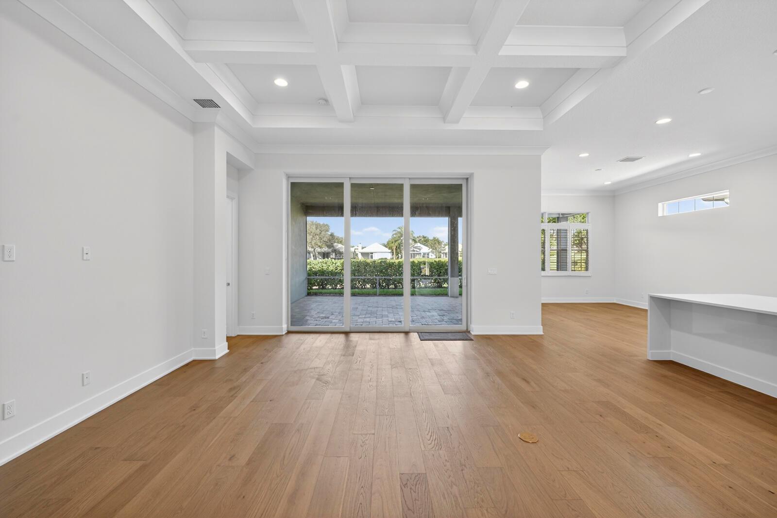 An empty living room features light wood flooring, a coffered ceiling, and sliding glass doors — VERO BEACH, FL