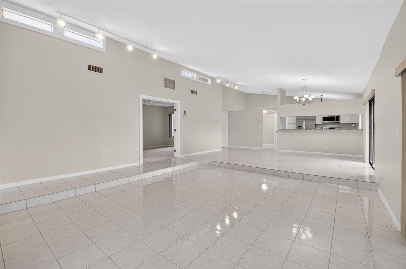 A spacious living area with light-colored tile flooring, vaulted ceilings, and a sunken floor section — 5580 Piping Rock Drive, Boynton Beach FL 33437, BOYNTON BEACH, FL