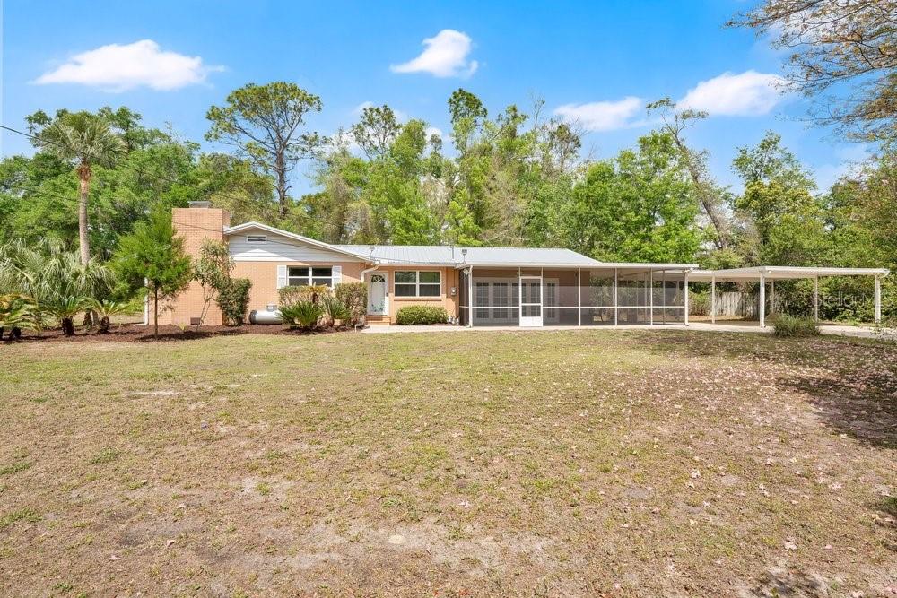 A single-story house with a brick chimney, screened-in porch, and attached carport on a lawn — 5137 MOUNT PLYMOUTH ROAD, APOPKA, FL