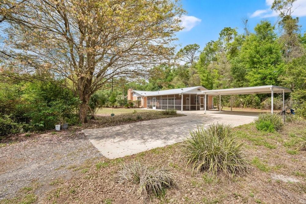 A single-story house with a screened-in porch and a detached carport sits among trees — 5137 MOUNT PLYMOUTH ROAD, APOPKA, FL