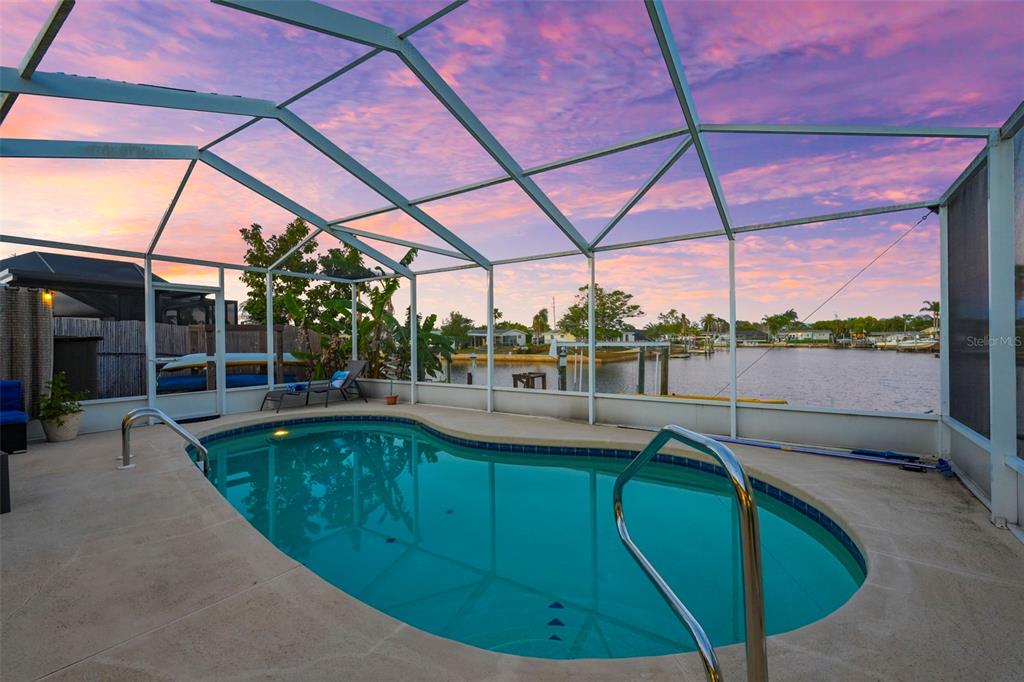 A screened-in swimming pool overlooks a canal at sunset — 12532 5TH ISLE, HUDSON, FL