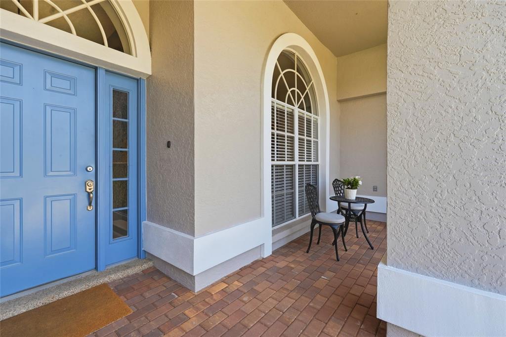 A blue front door opens onto a brick-paved porch with a small bistro set — 6130 55TH AVENUE CIRCLE E, BRADENTON, FL