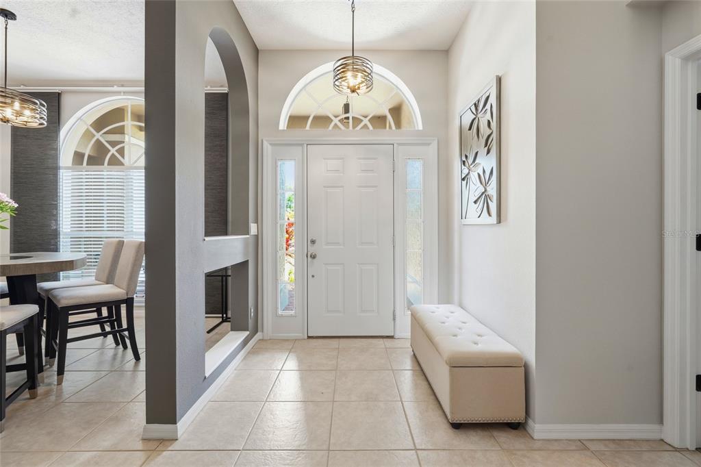 A bright entryway features a white front door with sidelights, tile flooring, and a bench — 6130 55TH AVENUE CIRCLE E, BRADENTON, FL