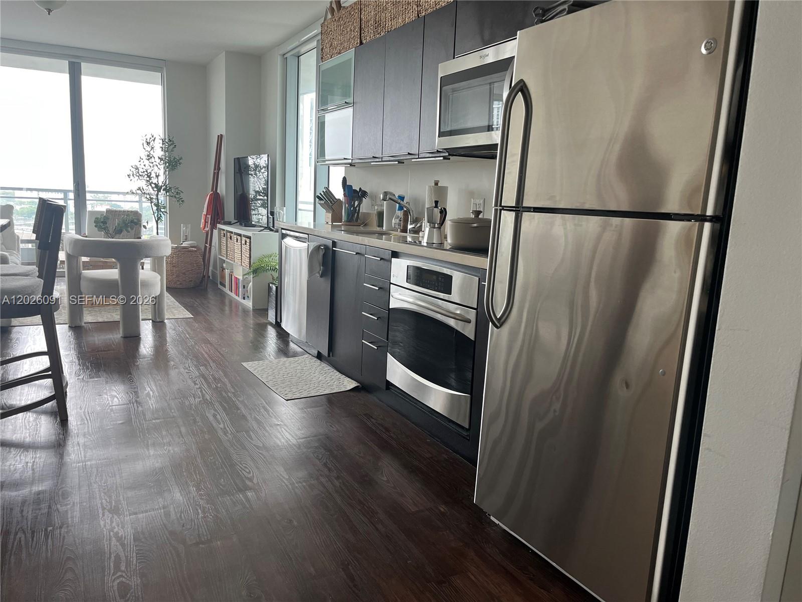 A modern kitchen with dark cabinets and stainless steel appliances overlooks a bright living area — 90 SW 3rd St # 1705, Miami FL 33130, MIAMI, FL