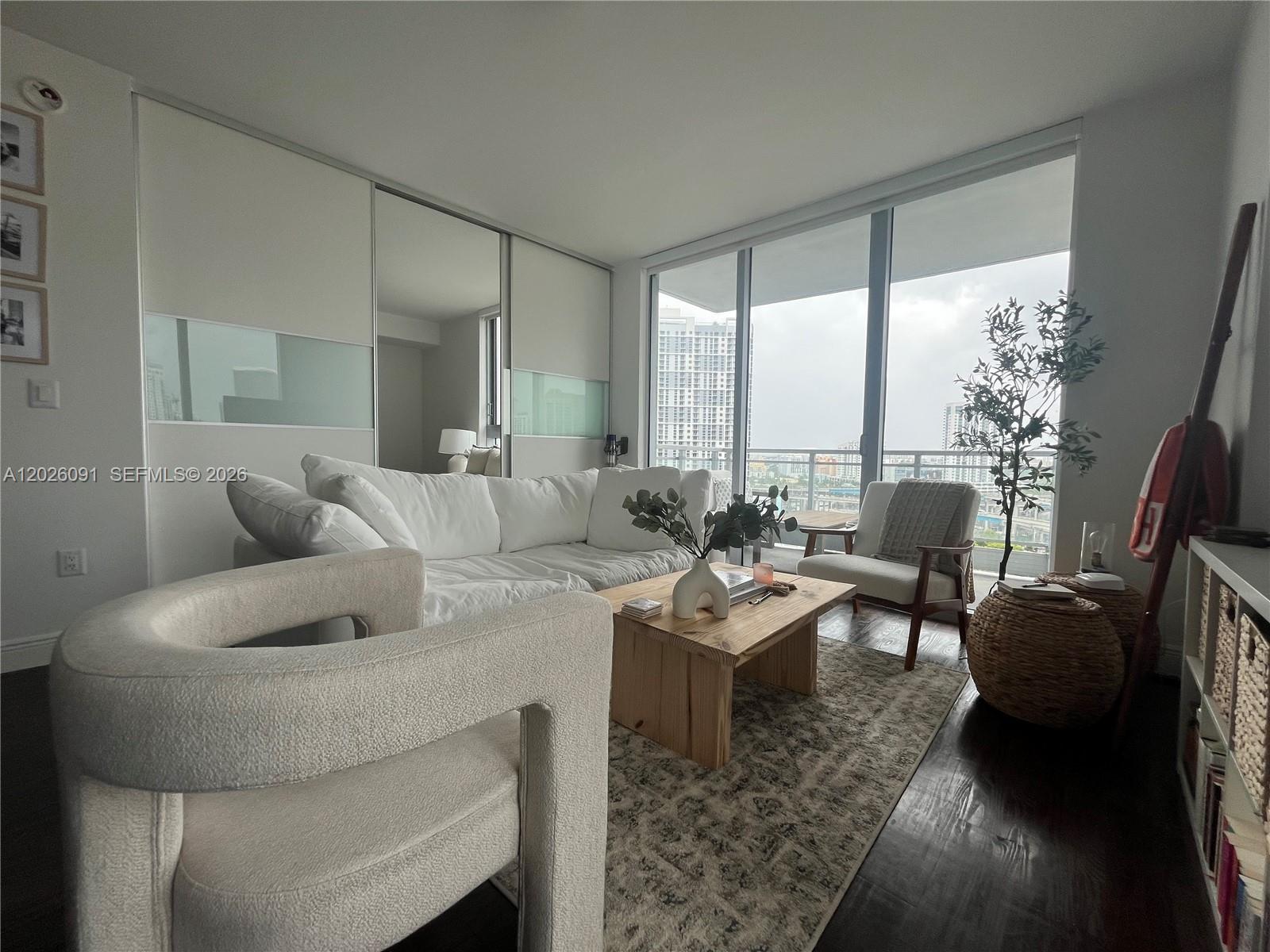 A living room features a white sectional sofa, a wooden coffee table, and floor-to-ceiling windows — 90 SW 3rd St # 1705, Miami FL 33130, MIAMI, FL