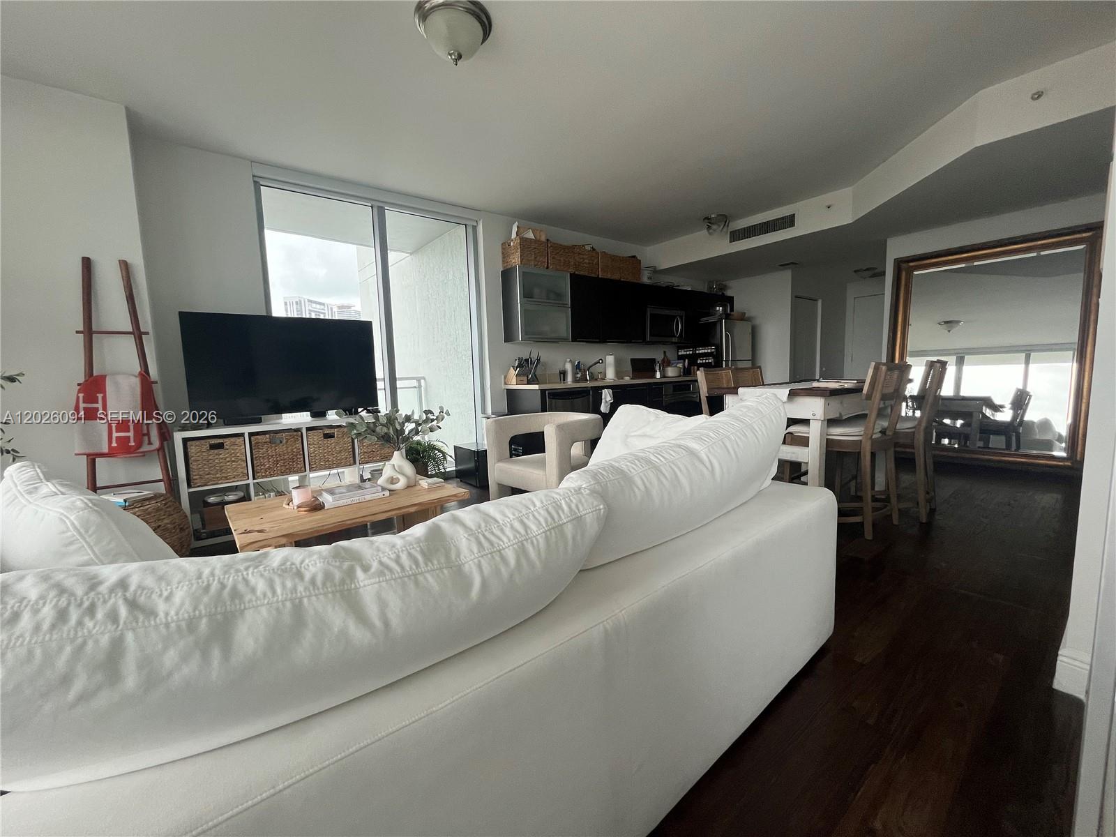 A living room and kitchen area features a white sofa, dark wood floors, and a balcony — 90 SW 3rd St # 1705, Miami FL 33130, MIAMI, FL