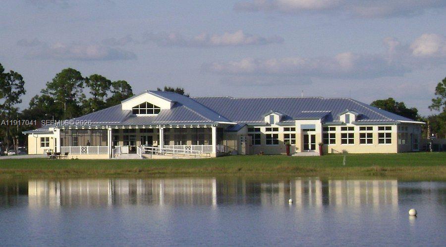 A single-story building with a metal roof sits beside a lake under a blue sky — 4525 MAJORCA DR, Sebring FL 33872, SEBRING, FL