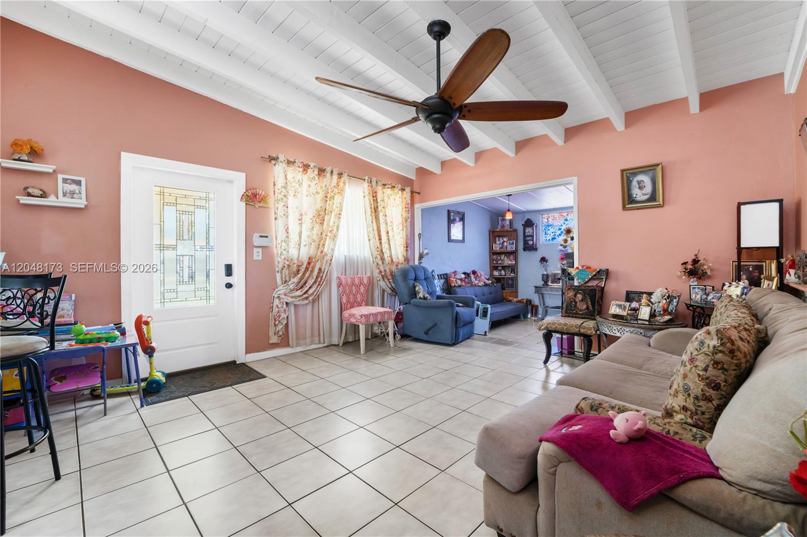 A living room with peach walls, white beamed ceilings, tile floors, and a ceiling fan — 1300 S 20th Ave, Hollywood FL 33020, HOLLYWOOD, FL