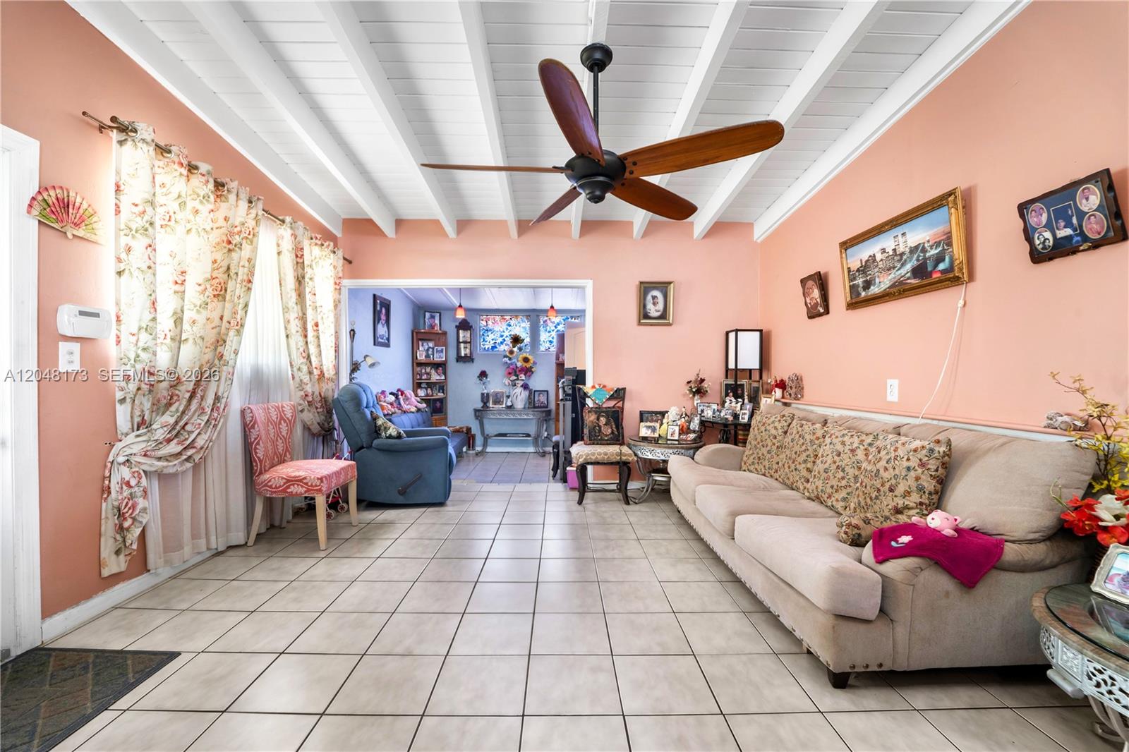 A living room features peach walls, a white beamed ceiling, tile flooring, and a ceiling fan — 1300 S 20th Ave, Hollywood FL 33020, HOLLYWOOD, FL