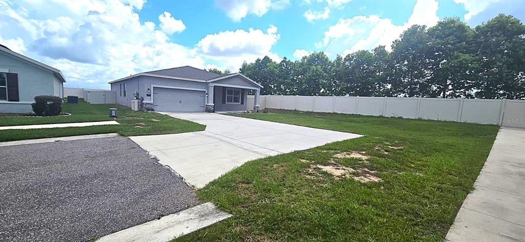A single-story house with a two-car garage and a white vinyl fence in the backyard — 212 BERGAMOT LOOP, DAVENPORT, FL