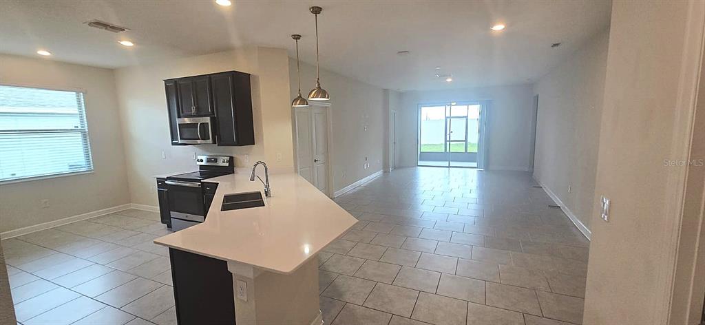 An open-concept kitchen with dark cabinets and a white island overlooks a tiled living area — 212 BERGAMOT LOOP, DAVENPORT, FL