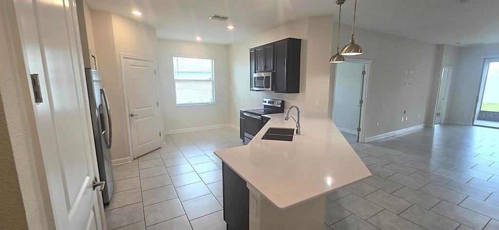 A kitchen features white countertops, dark cabinetry, stainless steel appliances, and light-colored tile flooring — 212 BERGAMOT LOOP, DAVENPORT, FL