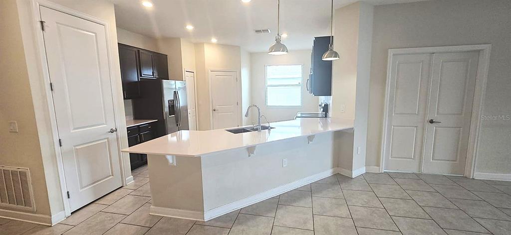 A kitchen features dark cabinets, a white island countertop, and light-colored tile flooring — 212 BERGAMOT LOOP, DAVENPORT, FL