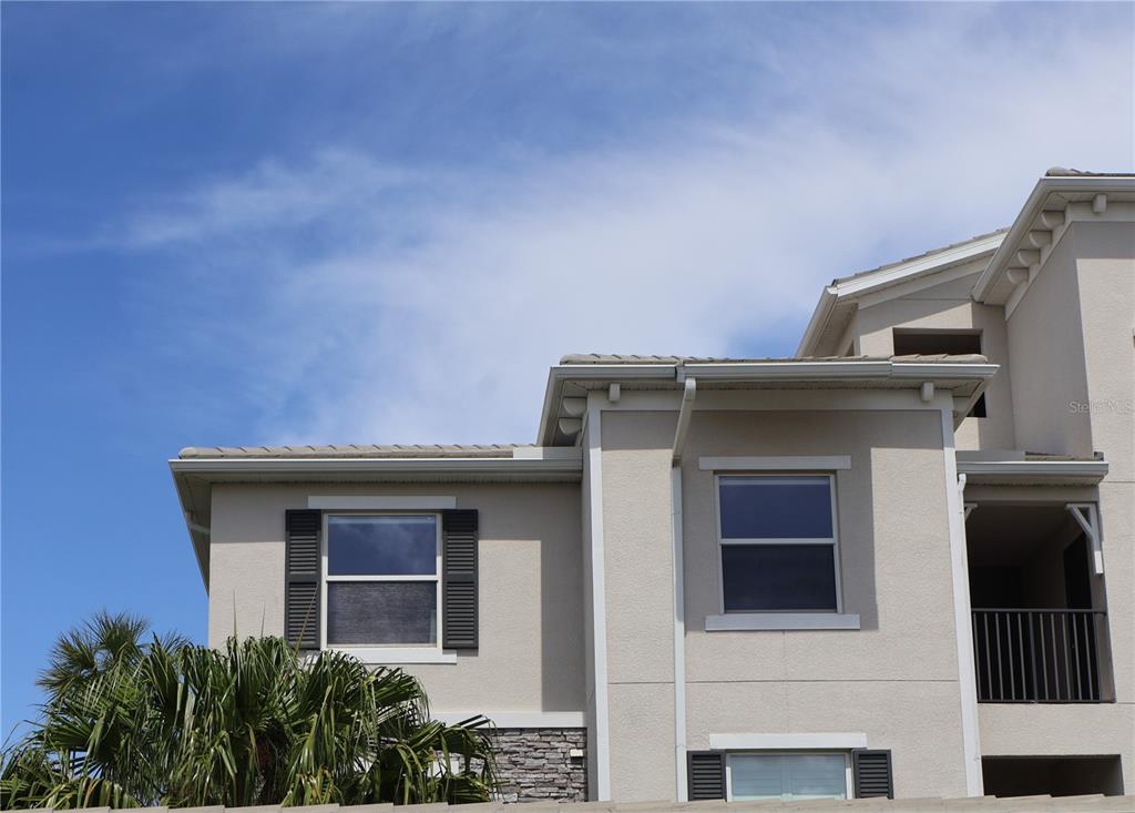 An exterior view of a multi-story stucco building with a tiled roof and palm tree — 920 TIDEWATER SHORES LOOP UNIT 301, BRADENTON, FL