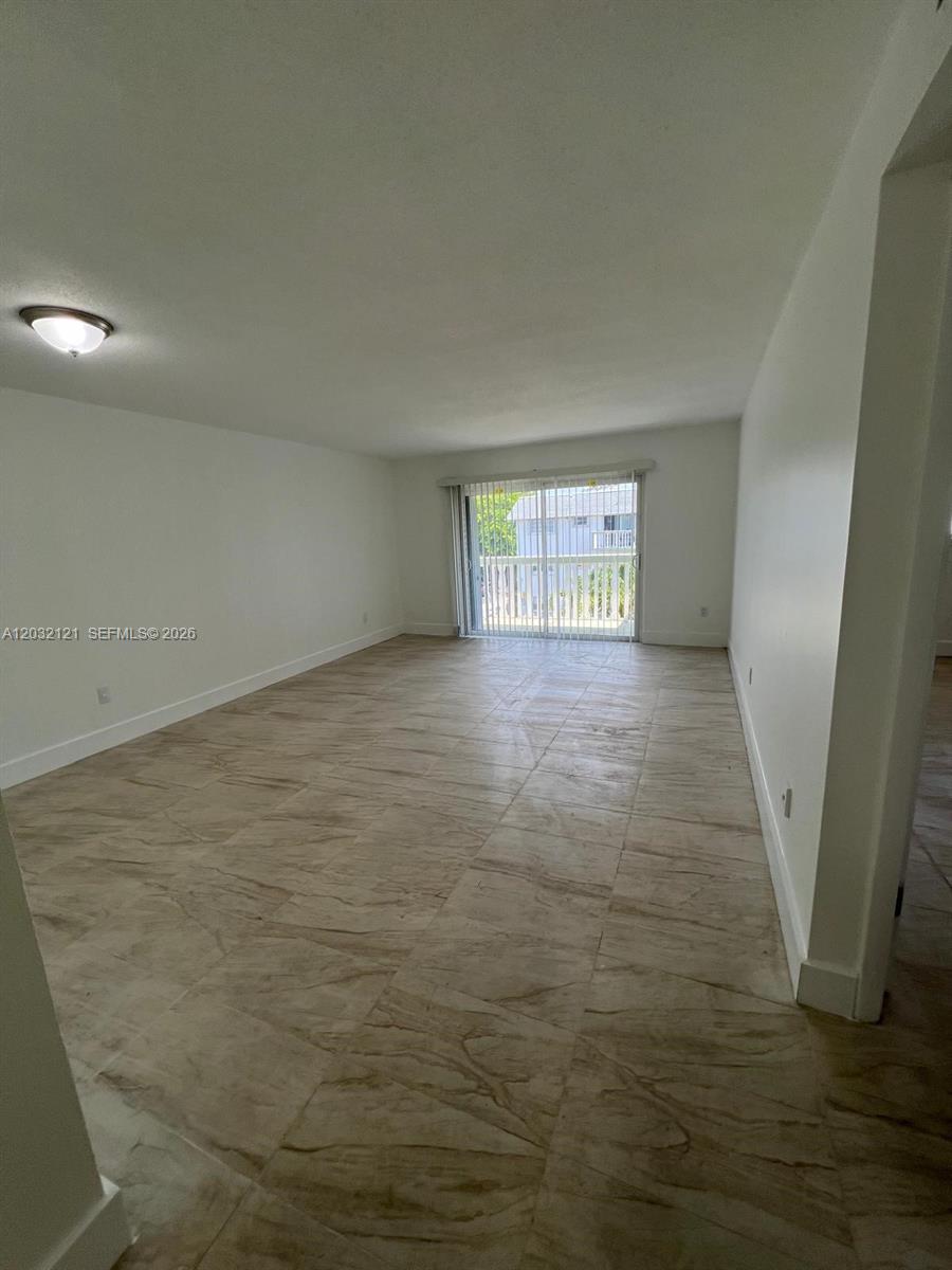 An empty room features light-colored tile flooring, white walls, and a sliding glass door — MIAMI, FL