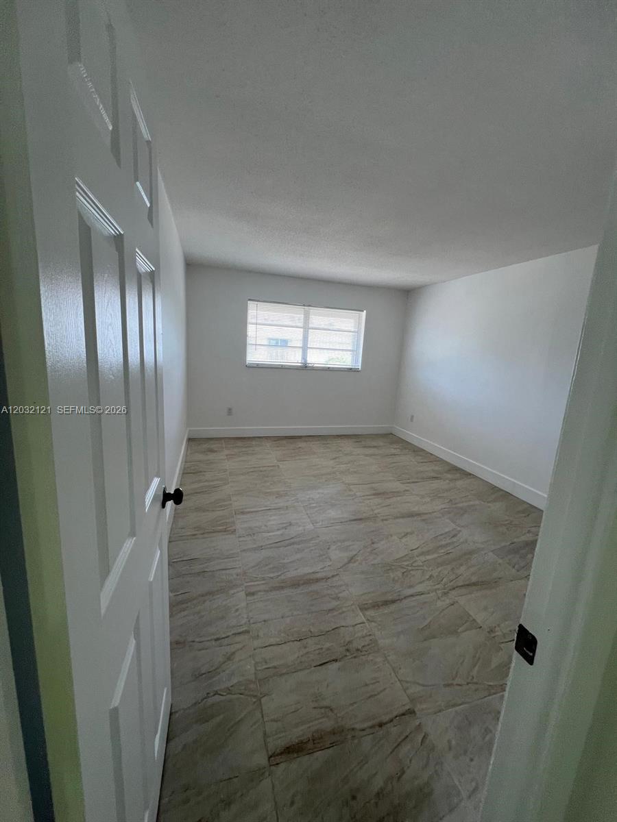 An empty room features white walls, a single window, and light-colored tile flooring — MIAMI, FL