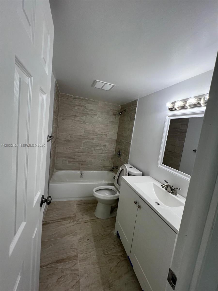 A bathroom features a white vanity, a toilet, and a bathtub with tiled walls — MIAMI, FL