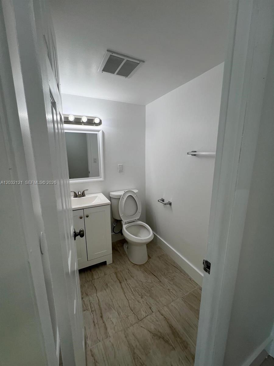 A small bathroom features a white vanity, a toilet, and light-colored wood-look tile flooring — MIAMI, FL