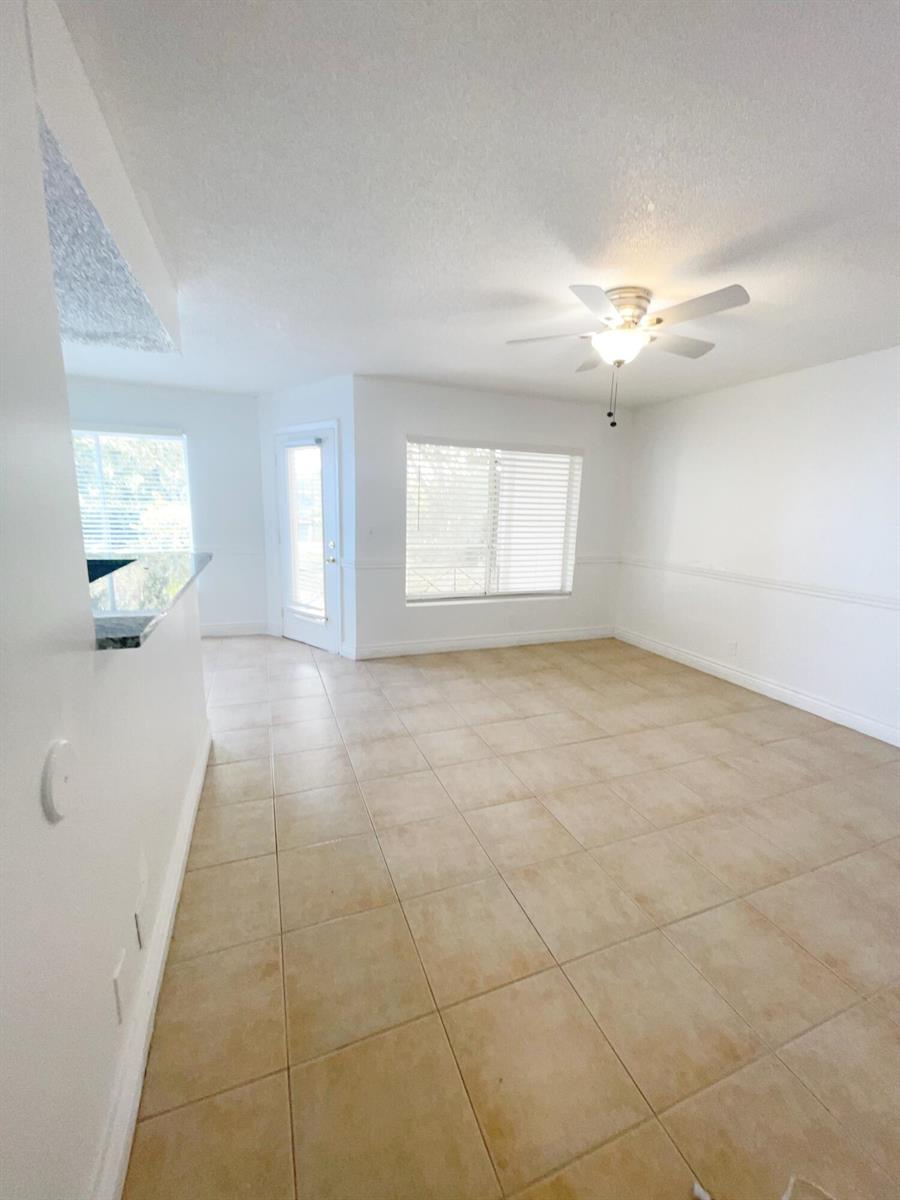An empty room with beige tile flooring, white walls, a ceiling fan, and large windows — 815 W Boynton Beach Boulevard # 102, Boynton Beach FL 33426, BOYNTON BEACH, FL