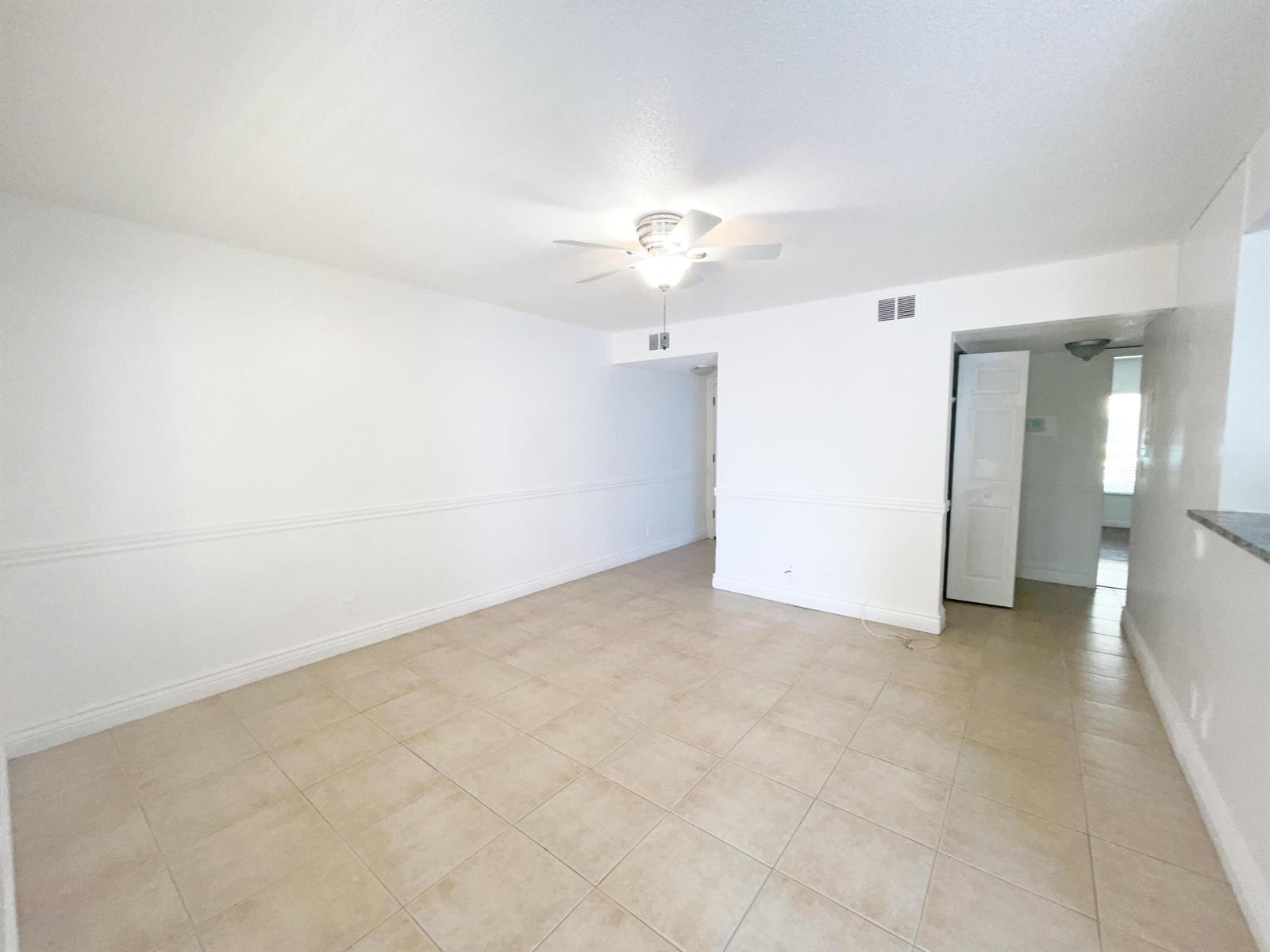 An empty room features white walls with chair rail molding and light-colored square floor tiles — 815 W Boynton Beach Boulevard # 102, Boynton Beach FL 33426, BOYNTON BEACH, FL