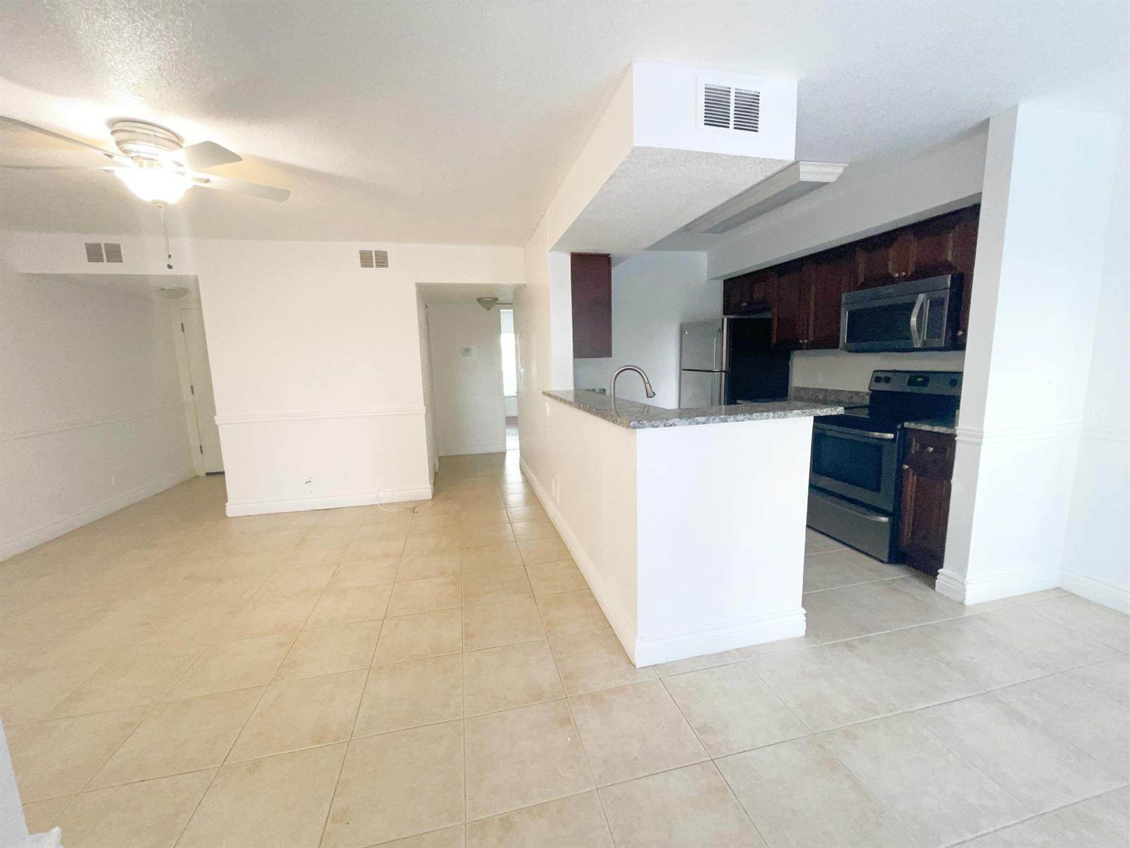 An open-concept kitchen with dark wood cabinets and a breakfast bar overlooks a tiled living area — 815 W Boynton Beach Boulevard # 102, Boynton Beach FL 33426, BOYNTON BEACH, FL
