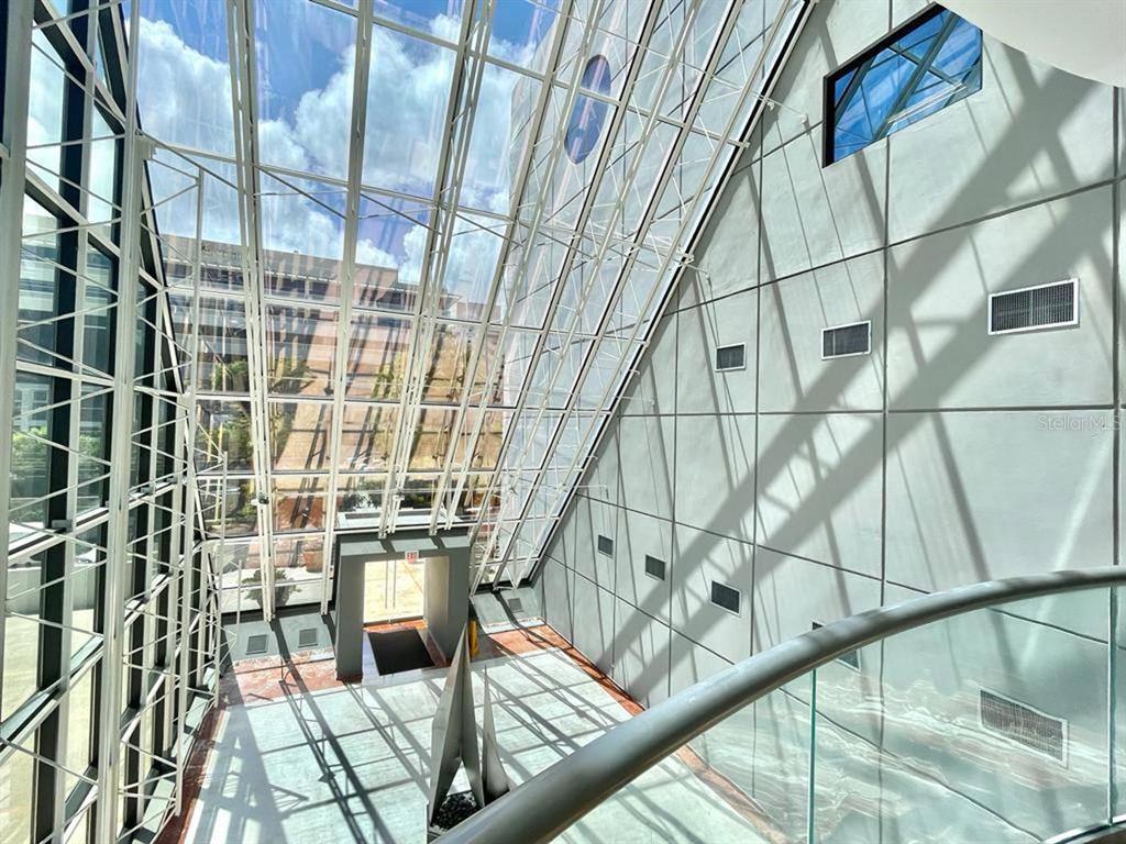 A high-ceilinged atrium features a glass-paneled roof, a metal staircase, and large gray wall panels — 1 CALLE 1, GUAYNABO, PR