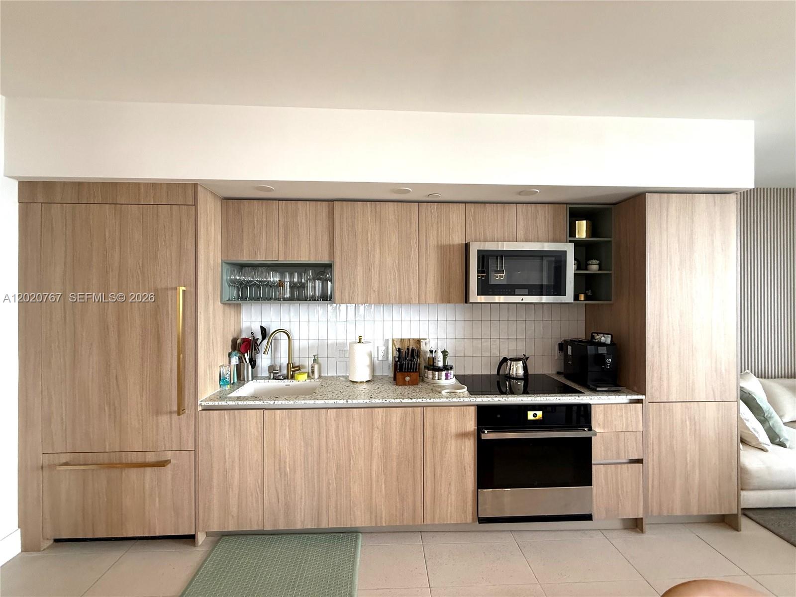 A modern kitchen features light wood cabinetry, a white tiled backsplash, and stainless steel appliances — 159 NE 6th St # 4016, Miami FL 33132, MIAMI, FL