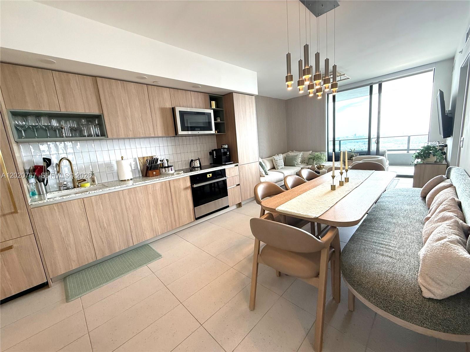 A modern kitchen and dining area features light wood cabinetry, tile flooring, and floor-to-ceiling windows — 159 NE 6th St # 4016, Miami FL 33132, MIAMI, FL