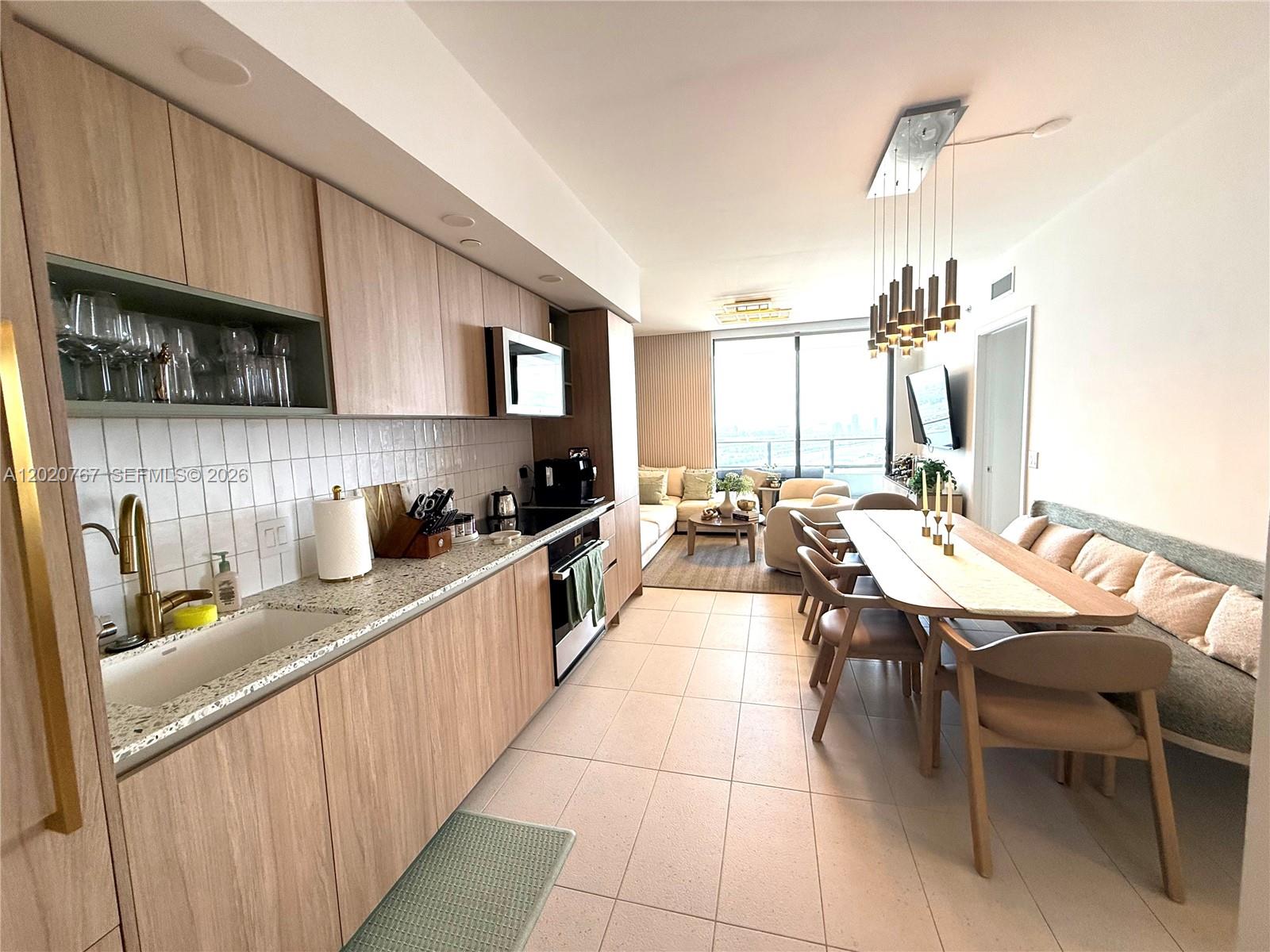 A modern kitchen with light wood cabinets and granite countertops opens into a dining area — 159 NE 6th St # 4016, Miami FL 33132, MIAMI, FL