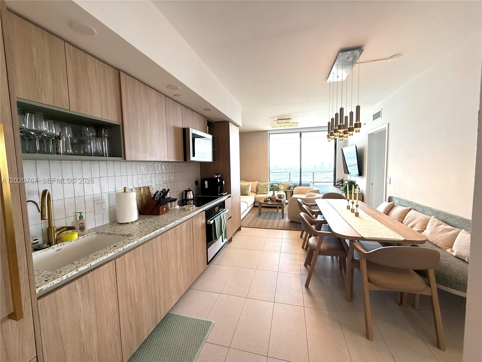 A modern kitchen and dining area feature light wood cabinets, tile floors, and city views — 159 NE 6th St # 4016, Miami FL 33132, MIAMI, FL