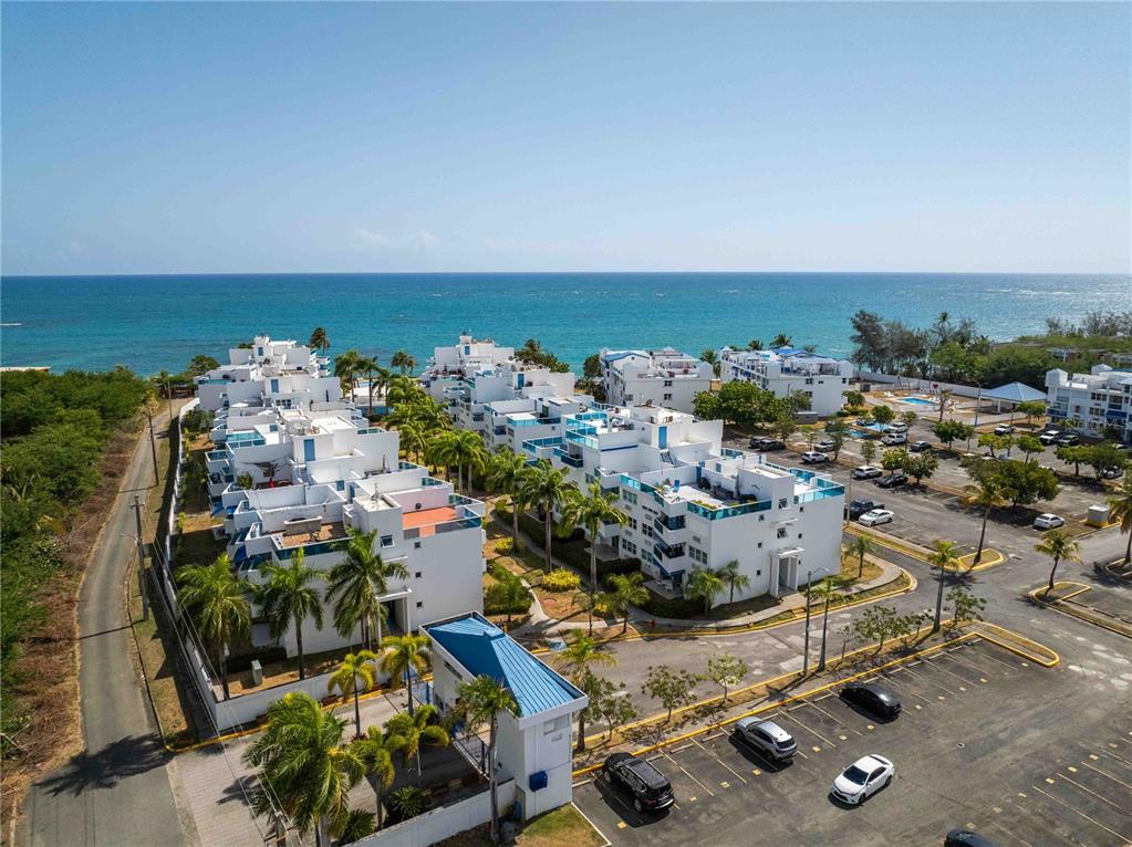 An aerial view shows a multi-story white apartment building with blue glass balcony railings — 1 CALLE EL CHARLIE UNIT CO-308, LOIZA, PR