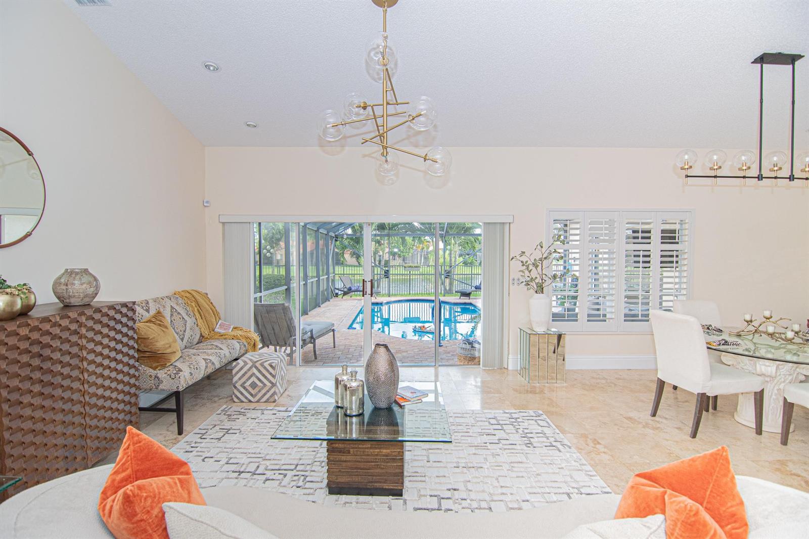 A living and dining area features a glass coffee table, modern chandeliers, and a pool view — 8410 Brussels Way, Boca Raton FL 33434, BOCA RATON, FL