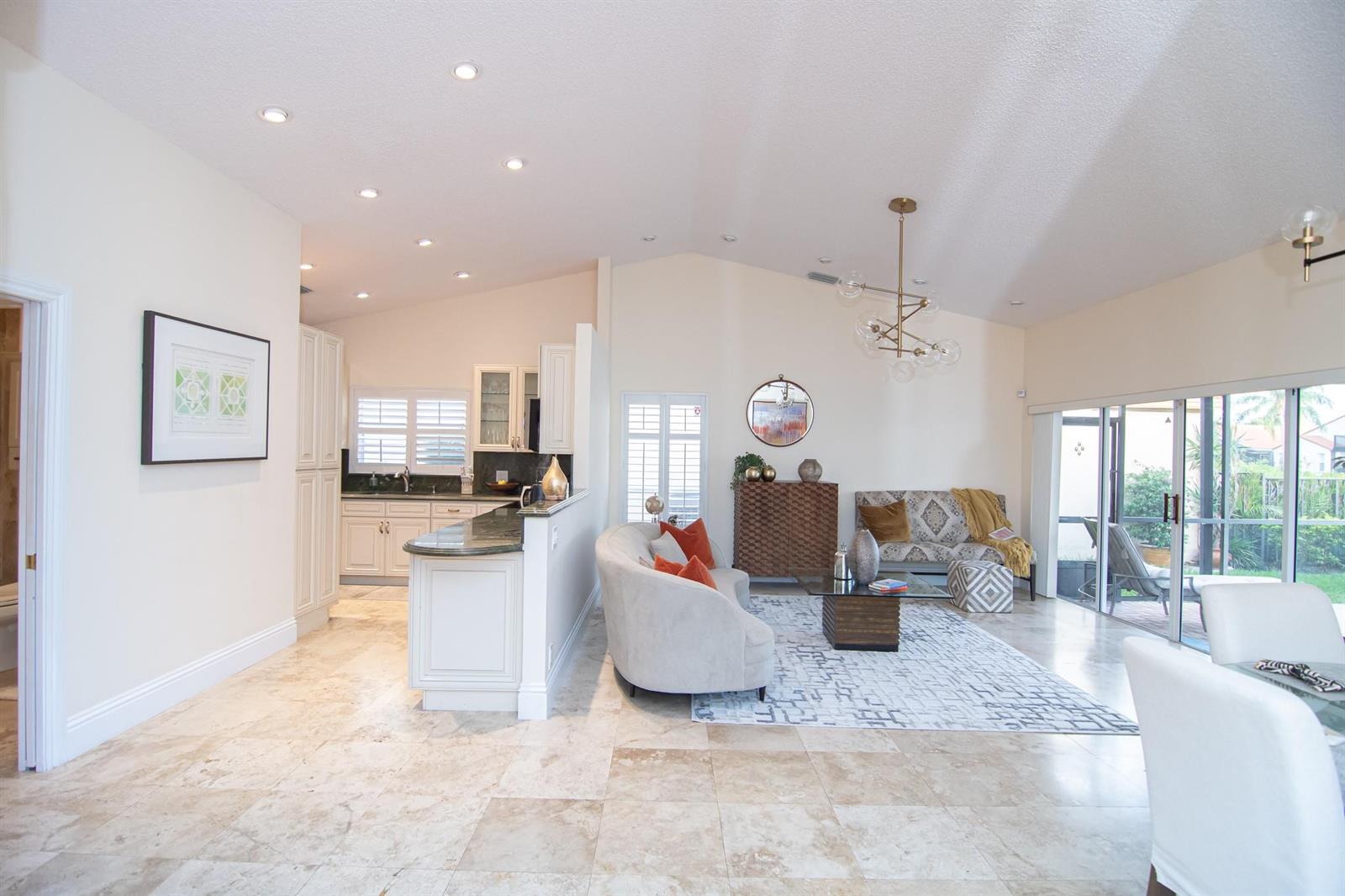 An open-concept living room and kitchen with tile flooring, vaulted ceilings, and sliding glass doors — 8410 Brussels Way, Boca Raton FL 33434, BOCA RATON, FL