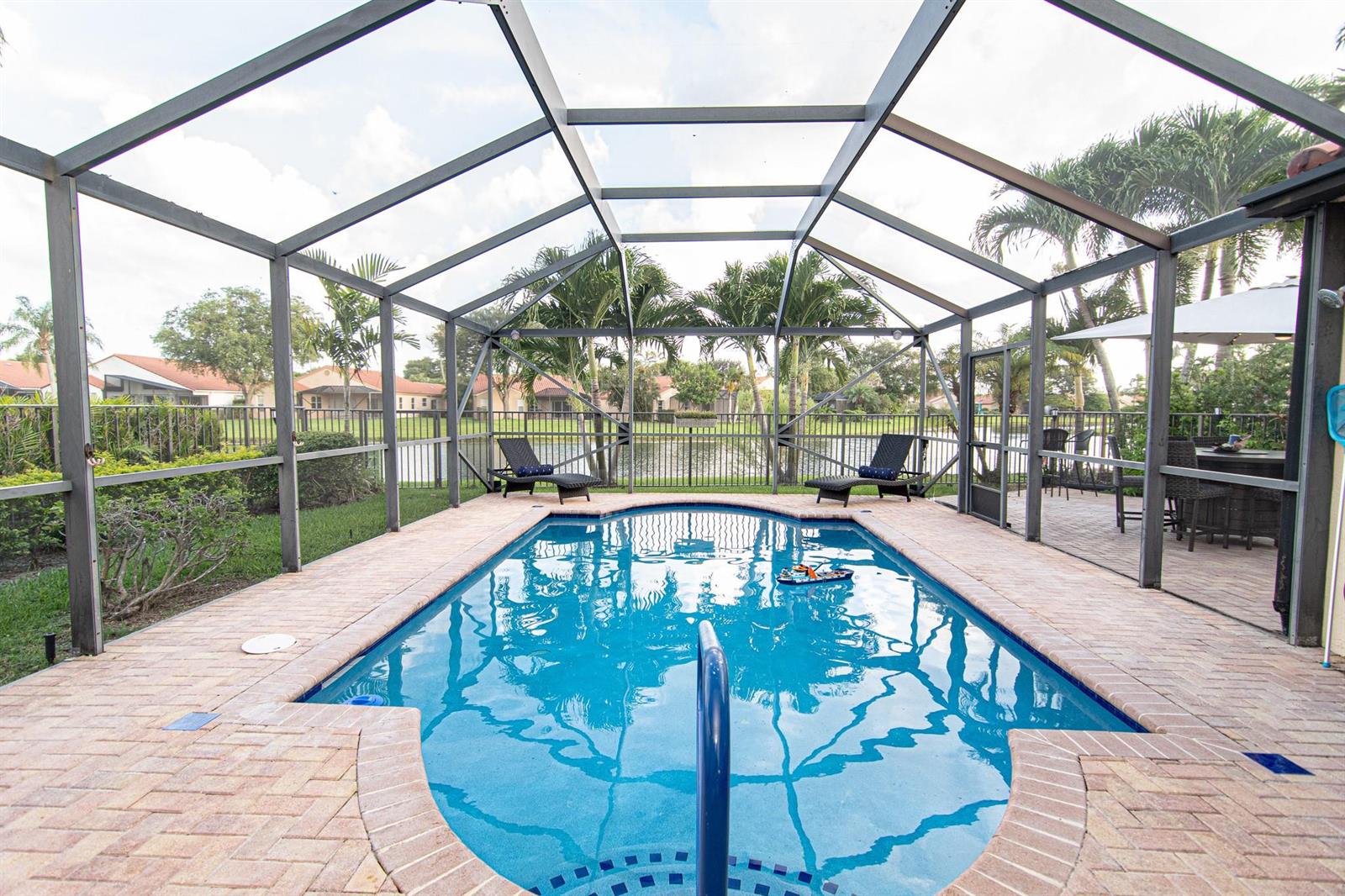 A screened-in swimming pool with a brick deck overlooks a lake and palm trees — 8410 Brussels Way, Boca Raton FL 33434, BOCA RATON, FL