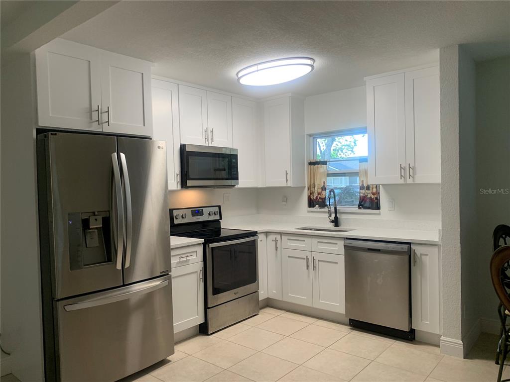 A kitchen features white cabinets, stainless steel appliances, and light-colored tile flooring — 7014 HERSHEY WAY, ORLANDO, FL